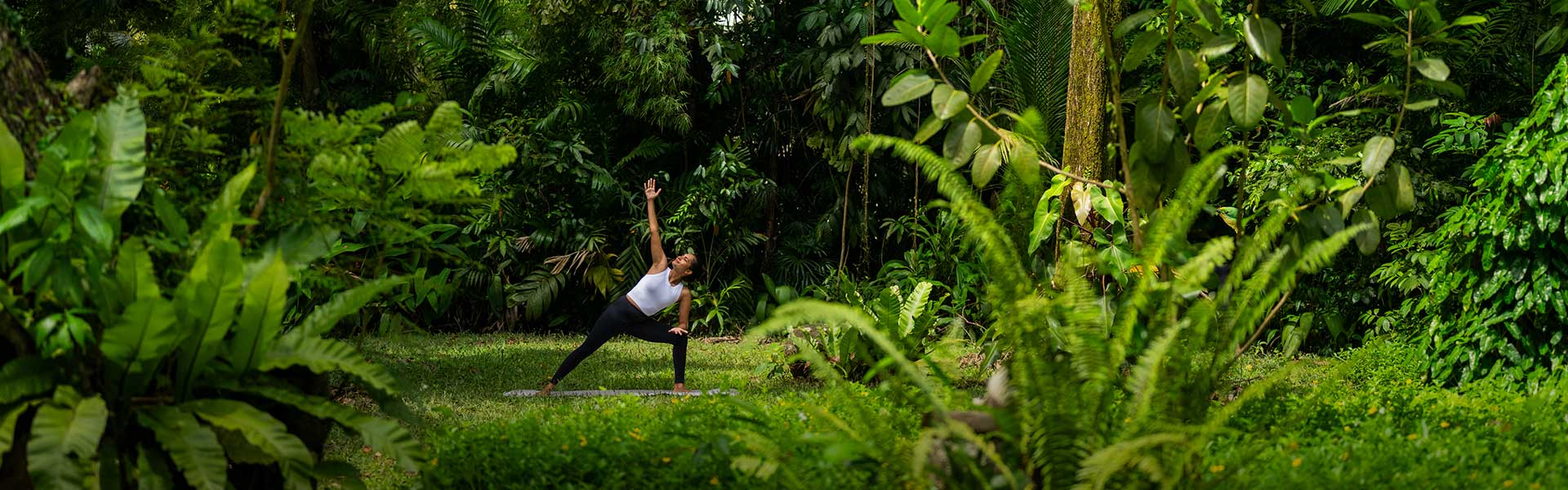 Woman practicing yoga amidst lush greenery at Teardrop Hotels, a luxury wellness hotel in Sri Lanka.